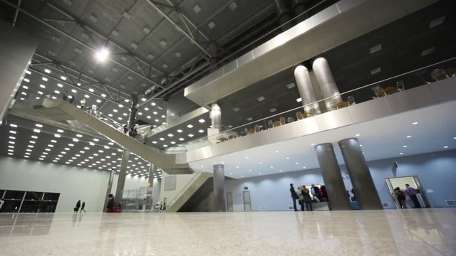 People walk in enormous silver hall with big stairs