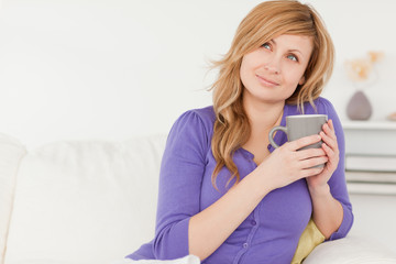 Pretty red-haired woman holding a cup of coffee while sitting on
