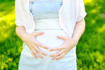 Young woman holding hands on her pregnant belly