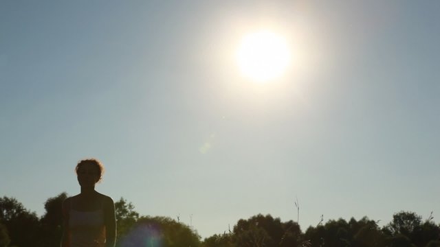 young woman walking in park, looking at sun and coming out