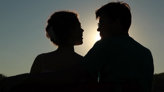 back view of embracing couple sits on bench and talks