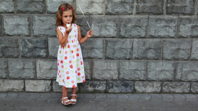 little girl stands against wall, eats ice cream