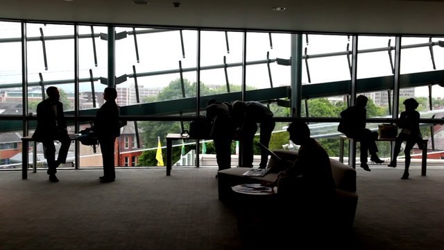 People standing near windows, man is sitting on sofa near table