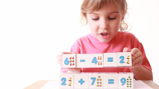 girl play wooden blocks with numbers, builds wall of cubes
