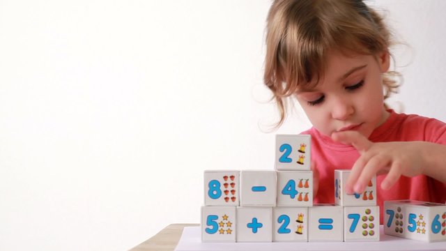 girl puts wooden bloks with numbers  on desk, adds cubes