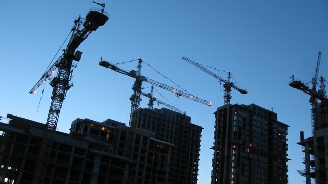 Crane silhouettes at construction site in evening, time lapse