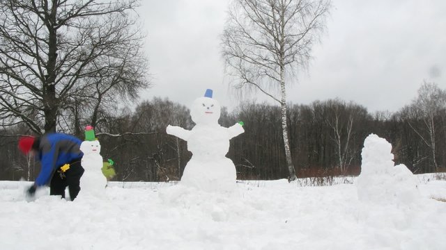 Two little kids and their dad sculpt three snowmans, time lapse