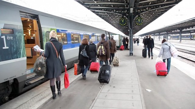people with luggage at station are walk on platform along train