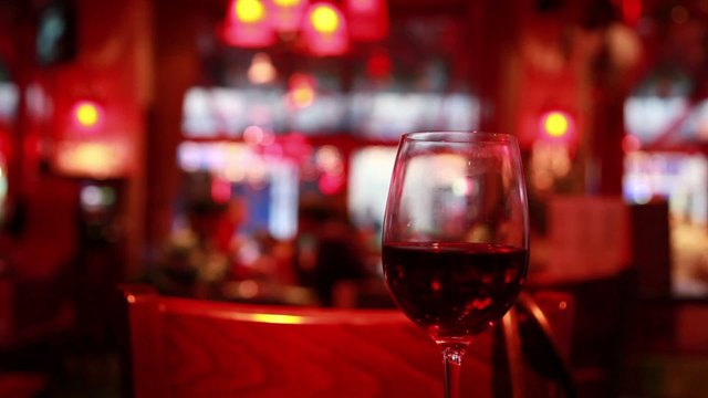 glass of red wine stands on table, backdrop hall of restaurant