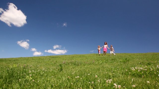 woman with children holding hands descend hill with grass
