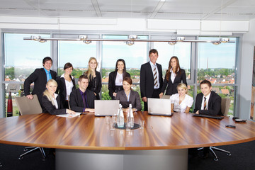Viele Geschäftsleute im Büro am großen Tisch mit Blick zur Kamera