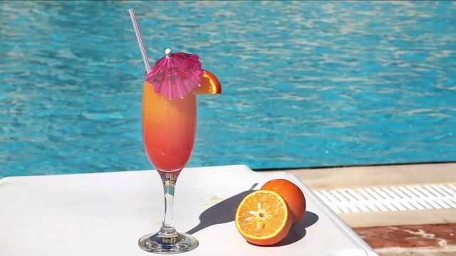 Orange cocktail with umbrella and straw near swimming pool