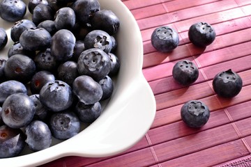 Blueberries in a white dish on a lilac wooden place mat