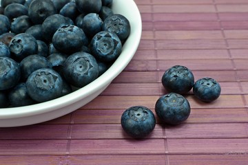 Blueberries in a white dish on a lilac wooden place mat