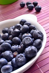 Blueberries in a white dish on lilac wooden place mat