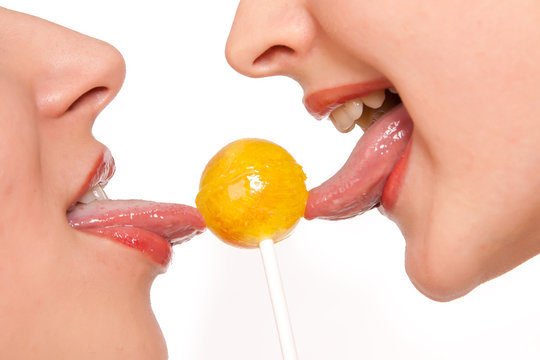 Two sweet female models kissing through lollipop