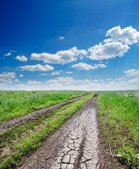 Obraz premium cracked rural road in green grass and cloudy sky