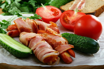 Sausages wrapped in bacon with vegetables and herbs.