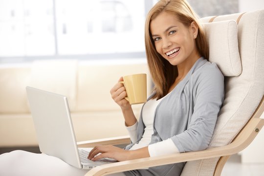Happy young woman with computer and coffee mug