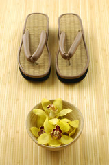 Wooden bowl of orchid with straw flip flops on mat
