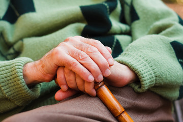 Elderly man sitting, resting his hands on a walking stick
