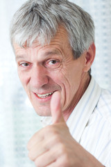 Closeup image of a happy aged man says OK holding finger up