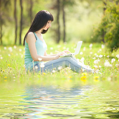 Cute woman with white laptop in the park with dandelions