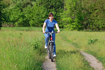 Naklejka premium Happy young woman on a green meadow riding a bicycle