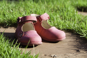 Детские и женские туфли на каменной плите в зеленой траве - obrazy, fototapety, plakaty