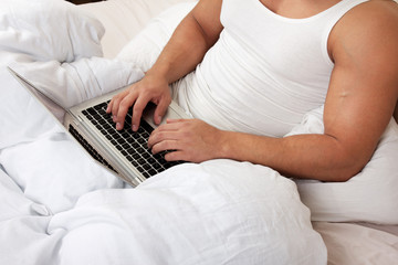 Man using laptop, sitting on bed