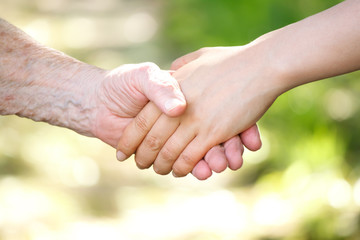 Senior and young women holding hands over shiny green background