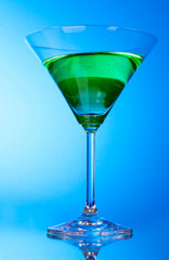 glass with a green alcoholic beverage on blue background