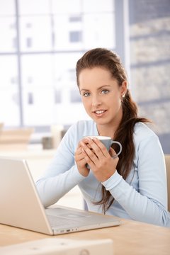 Attractive woman using laptop at home drinking tea