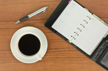 Top view of notebook and pen with coffee on table