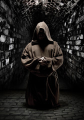 Praying monk in dark temple corridor - obrazy, fototapety, plakaty
