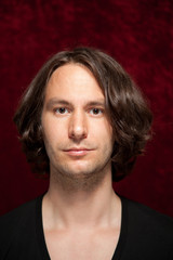 Junger Mann mit langem braunem Haar vor rotem Hintergrund