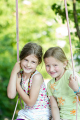 Two happy girls together on the swing - playing outdoor