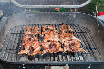 BBQ quails cooking on a grill in the garden