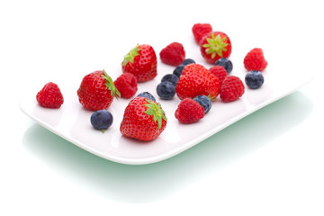 Weißer Teller mit Erdbeeren, Himbeeren und Heidelbeeren