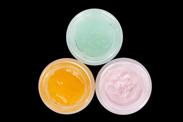 Three pots of skin care colored lotion.