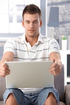 Young man staring at laptop screen horrified