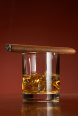 Whiskey with ice cubes and cigar, on brown