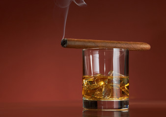 Whiskey with ice cubes and cigar, on brown