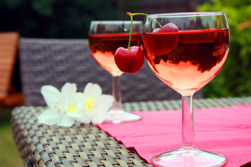 Weingläser mit Kirschen und Blumen im Freien