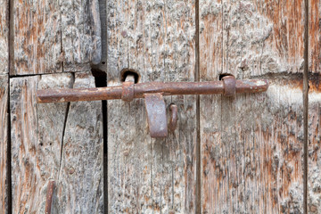 Металлическая задвижка на старых деревянных воротах.