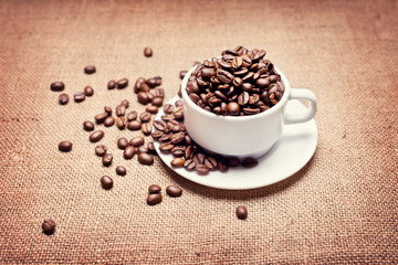 cup with coffee beans on fabric texture background
