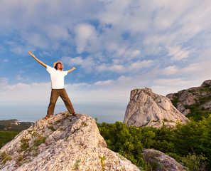 hiker at the top of a rock with his hands up enjoy sunny day