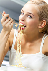 Happy smiling young blond woman eating spaghetti indoors