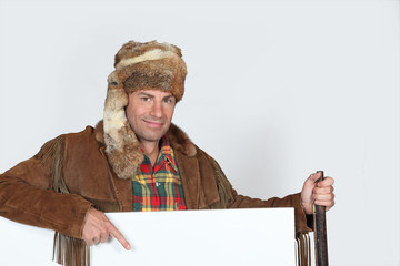 Man wearing a fur hat pointing to a blank poster