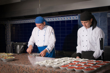 Two cooks preparing appetizers at commercial kitchen.